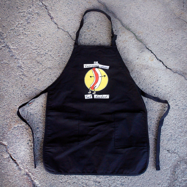 Image of the front of a black apron lying against a grey cracked asphalt background. background. It says "The lawrence arms" in black cursive on top of a white rectangle. Below that is a circle that is filled in with yellow color. Inside of the circle is a graphic of a hot dog with arms and legs and a smiley face on it. Below that it says Get fucked! In black text on top of white rectangles.