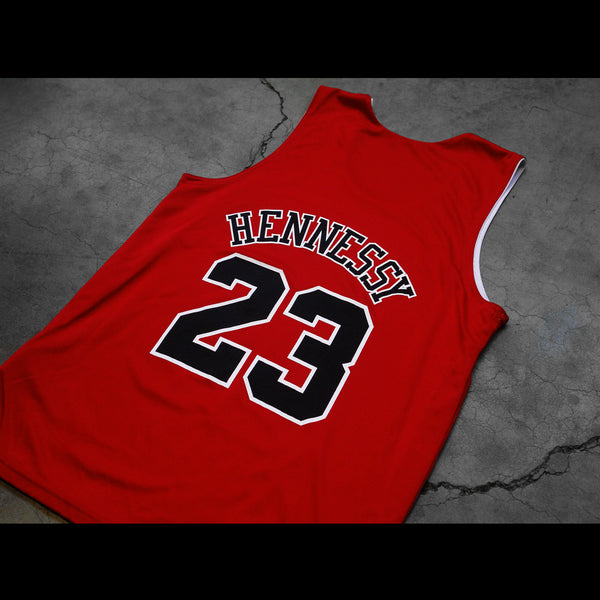Close up image of a red sleeveless jersey against a grey background. The back of the jersey says hennessy in black text with a white outline. The number 23 in black with a white outline is below that.