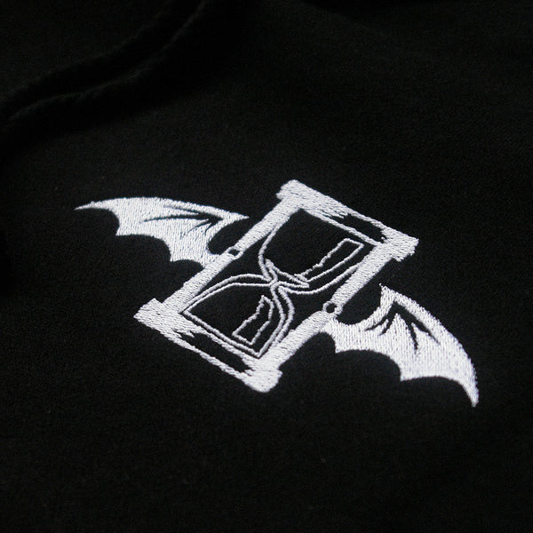 close up shot of the white embroidery of the hourglass with bat wings on a black hoodie