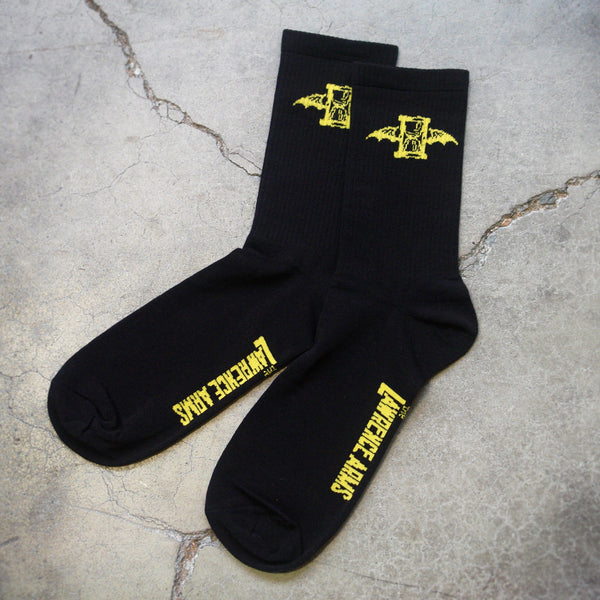 Image of black socks lying on a grey cracked background. The top of the socks have a yellow the lawrence arms logo on them which is an hourglass with wings. The bottom of the socks in yellow text say the lawrence arms.